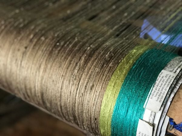 The disordered silk filaments are manually strung onto the loom's warp beams.&nbsp;